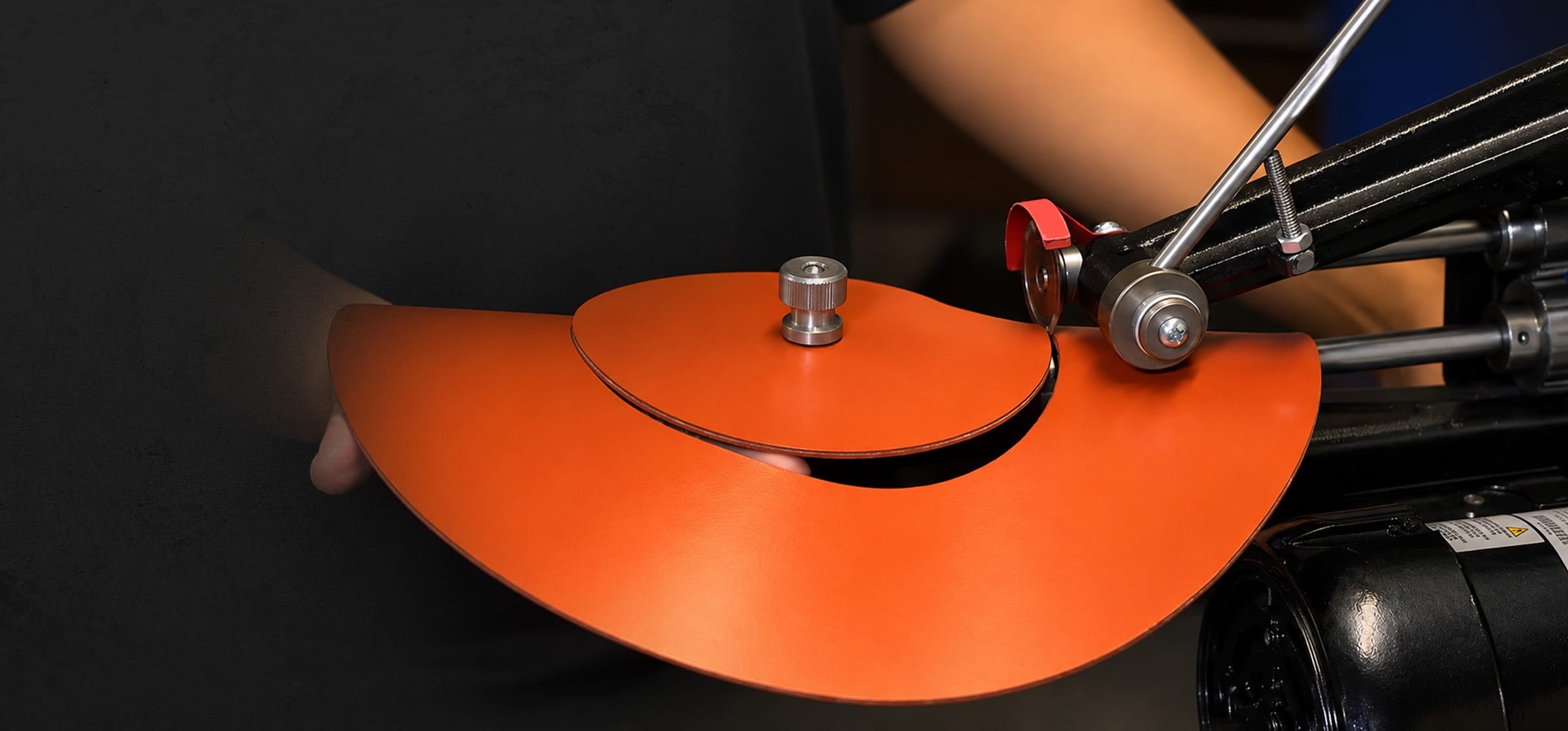A close-up of a person cutting an orange gasket with a rotary-cutter.