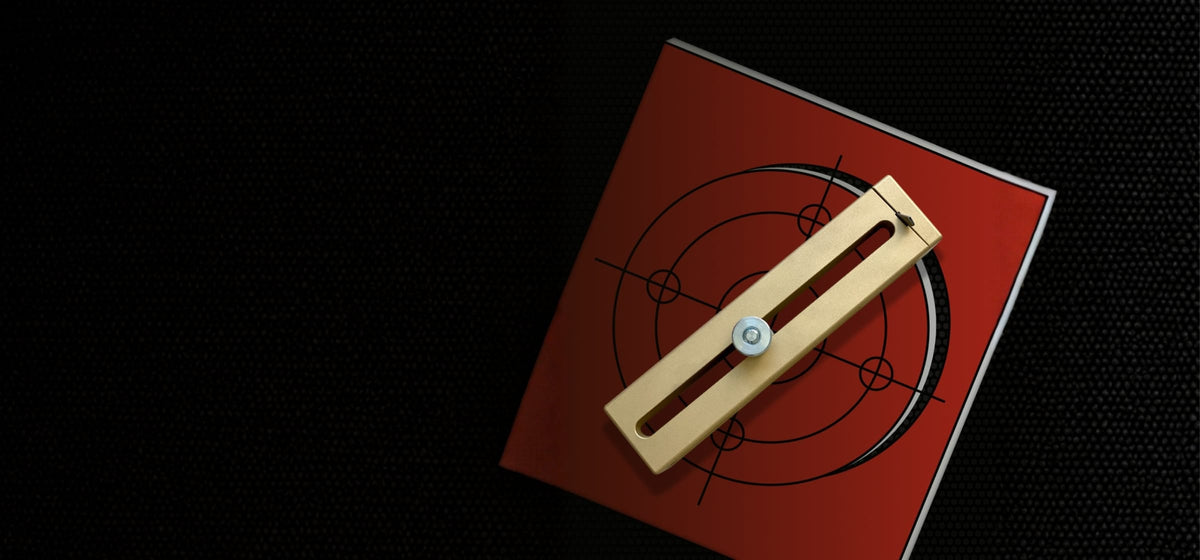 A brass cutter block with a metal center pin, resting diagonally on red gasket material partially cut.